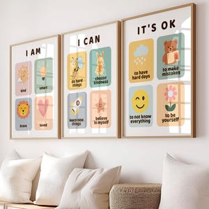 Puede incluir: Tres impresiones artísticas enmarcadas con mensajes inspiradores. La primera impresión dice "I AM" con palabras como "amable" y "valiente". La segunda dice "I CAN" con frases como "hacer cosas difíciles". La tercera dice "IT'S OK" con frases como "tener días difíciles".