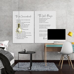 May include: Two white framed prints with black text of The Ten Commandments and The Lord's Prayer hang on a gray wall. A desk with a computer, yellow lamp, and white chair is to the right. A bed with a gray comforter is on the left.