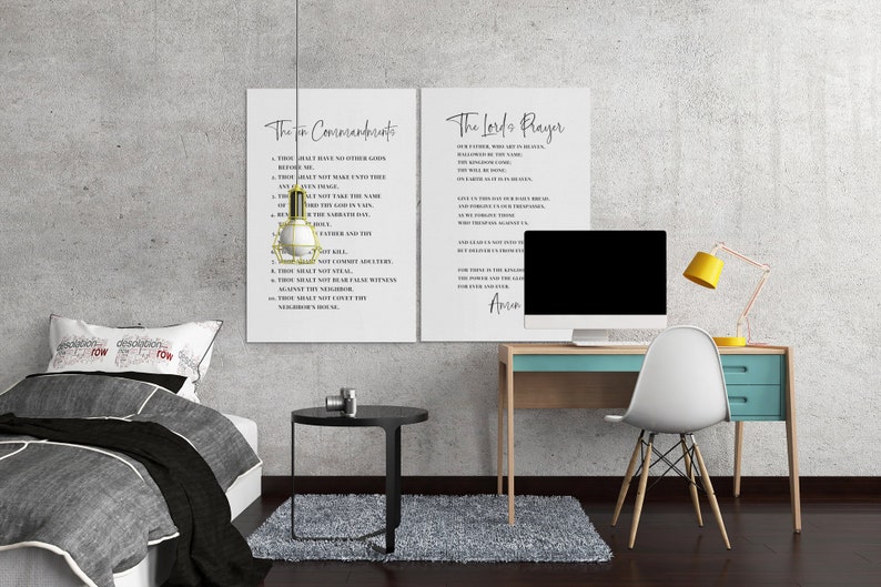 May include: Two white framed prints with black text of The Ten Commandments and The Lord's Prayer hang on a gray wall. A desk with a computer, yellow lamp, and white chair is to the right. A bed with a gray comforter is on the left.
