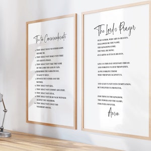 May include: Two framed prints with the text "The Ten Commandments" and "The Lord's Prayer" in elegant black script on a white background. The frames are light wood, and the prints are displayed on a wooden surface.