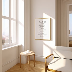 May include: A white framed print with the text "Armor of God" and a list of spiritual armour. The print is hanging on a white wall in a room with a wooden floor, a white armchair, and a small wooden table with a book and a white object on top.