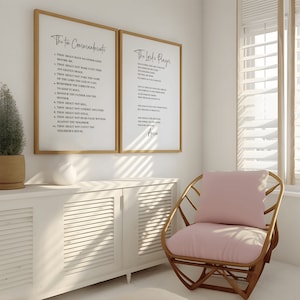 May include: Two framed prints on a white wall, one with "The Ten Commandments" and the other with "The Lord's Prayer" in black script. A light wood chair with a pink cushion sits nearby. A white cabinet and a potted plant are also in the room.
