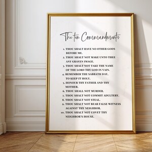 May include: A framed print featuring "The Ten Commandments" in elegant script. The text is displayed on a white background within a gold frame. The print is displayed against a white wall with molding.