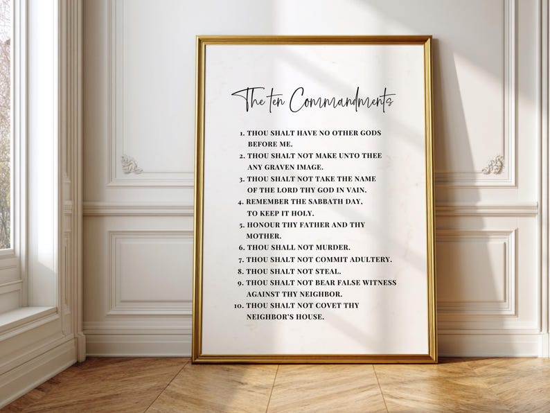 May include: A framed print featuring "The Ten Commandments" in elegant script. The text is displayed on a white background within a gold frame. The print is displayed against a white wall with molding.
