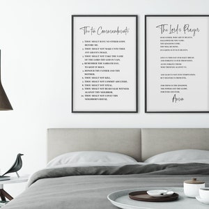 May include: Two framed prints with black frames and white backgrounds. The left print displays "The Ten Commandments" in elegant script, while the right print features "The Lord's Prayer." The prints are displayed above a bed with a neutral-toned headboard.