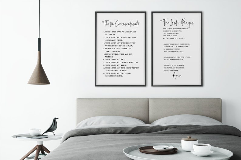 May include: Two framed prints with black frames and white backgrounds. The left print displays "The Ten Commandments" in elegant script, while the right print features "The Lord's Prayer." The prints are displayed above a bed with a neutral-toned headboard.