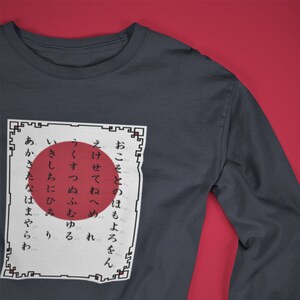 May include: A dark gray long-sleeve shirt with a white square featuring Japanese text and a red circle in the center. The text reads: "おこそとのほもよろをん えけせてねへめれ うくすつぬふむゆる いきしちにひみ り あかさたなはまやらわ"