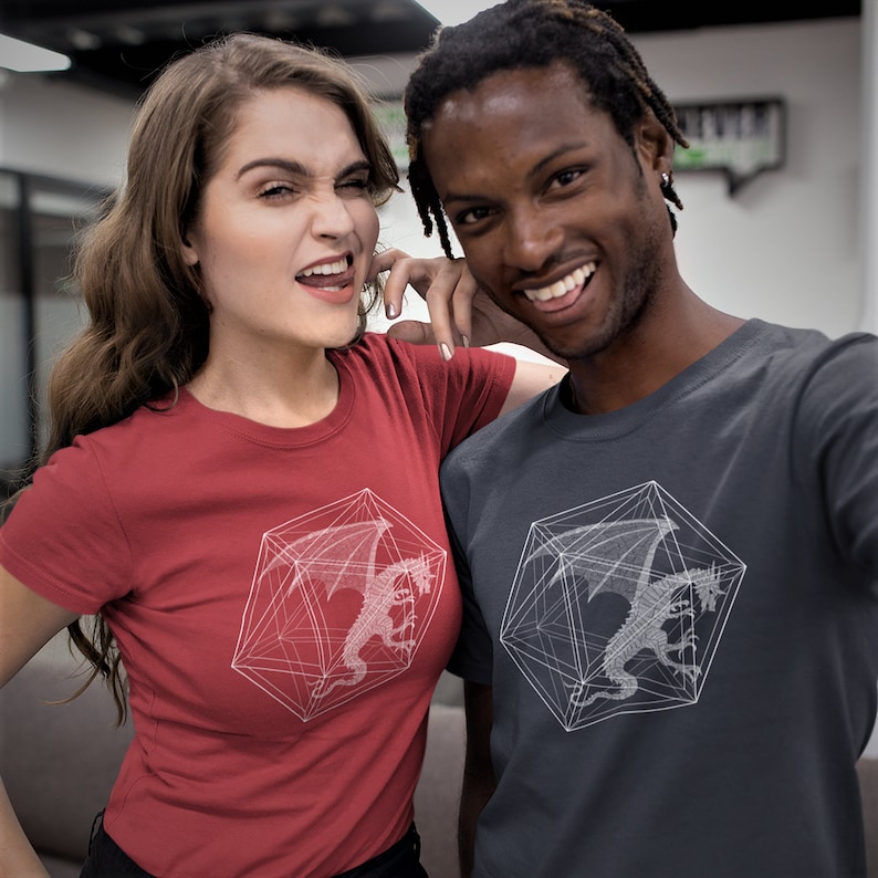 May include: Two people wearing red and gray t-shirts with a white graphic of a dragon inside a geometric shape. The graphic is a stylized representation of a twenty-sided die.