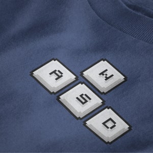 May include: A blue t-shirt with a white pixelated design of the word "FOMO" made to look like computer keys.