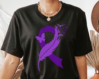 Może przedstawiać: Czarny T-shirt z wzorem fioletowej wstążki i pióra. Wstążka jest zawiązana w kokardę i ma motyla w środku. Pióro unosi się za wstążką.