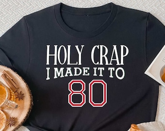 May include: Black t-shirt with white text that reads "HOLY CRAP I MADE IT TO 80" with the number 80 in red.