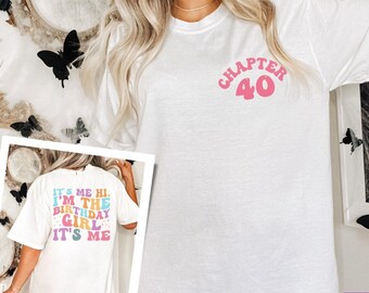 Puede incluir: Camiseta blanca con texto rosa que dice "Capítulo 40". La camiseta la lleva puesta una persona con el pelo largo y rubio. La parte de atrás de la camiseta tiene texto de colores que dice "It's me hi. I'm the birthday girl. It's me."