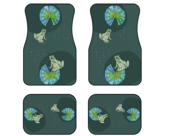 May include: Set of four car floor mats featuring a whimsical design. The mats have a dark teal background with illustrations of frogs on lily pads. The frogs are green and white, and the lily pads are blue and green. The mats are designed to protect the car's interior.