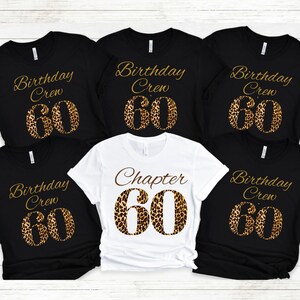 May include: Five t-shirts arranged in a group. Four black shirts feature the gold text Birthday Crew above a large leopard print number 60. One white shirt in the center features the brown text Chapter above a large leopard print number 60.