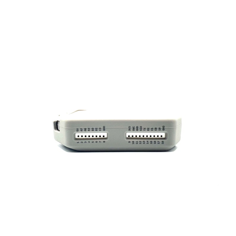 Op de afbeelding: Een lichtgrijs elektronisch apparaat met twee rijen pinconnectoren. Elke rij heeft genummerde pinnen. Het apparaat heeft tekstlabels boven de pinnen. De achtergrond is wit.