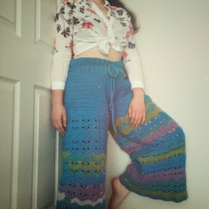 May include: Blue crochet trousers with a floral pattern and a tie waist. The trousers have a wide leg and a flowing silhouette.