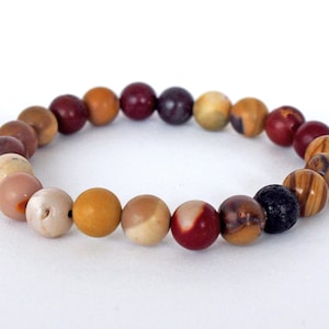 Peut inclure: Un bracelet composé de perles multicolores avec une variété de pierres, dont du rouge, du brun, du jaune et du blanc. Le bracelet comprend également une perle de lave noire.