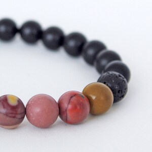 Peut inclure: Un bracelet de perles composé de pierres naturelles. Il comprend de l'onyx noir, de la pierre de lave et du jaspe de différentes couleurs, notamment rouge, rose et marron. Les perles rondes sont enfilées ensemble.