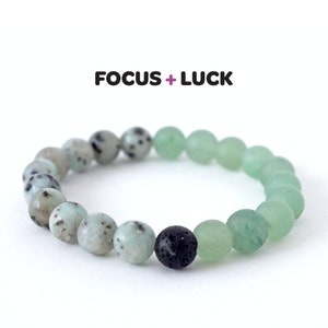 May include: A green and white beaded bracelet with a black lava bead. The bracelet has the words "FOCUS + LUCK" printed on it.
