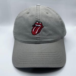 May include: Gray baseball cap with a red and white embroidered tongue logo. The cap has a curved brim and a six-panel design. The hat is made of a durable fabric and features a classic, adjustable fit.
