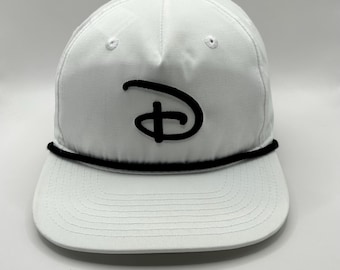 May include: A white baseball cap featuring a black embroidered Disney logo on the front panel. The cap includes a flat brim and a black rope detail running horizontally across the base of the crown, just above the brim, with a top button.