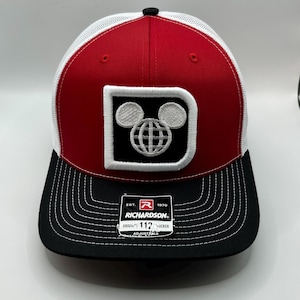 May include: A red and black baseball cap with white mesh back panels. The front features a white-bordered black patch with a white letter D and a globe icon with mouse ears. A Richardson 112 adjustable sticker is on the black brim.