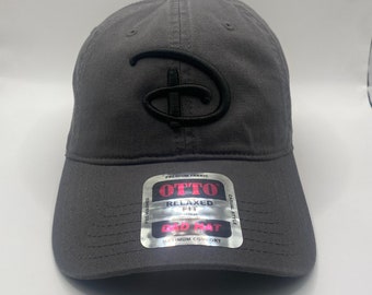 May include: A gray baseball cap with a black embroidered Disney logo. The cap has a relaxed fit and is labeled "Otto Dad Hat" with "Premium Fabric" and "Maximum Comfort" printed on the label.