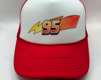 May include: A red and white trucker hat featuring a graphic print on the front panel. The design includes a yellow lightning bolt symbol next to the number 95 in orange and black, with a red and orange rectangular shape extending to the right.
