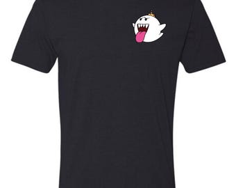 May include: A black short-sleeved t-shirt featuring a small graphic on the upper left chest. The graphic depicts a white ghost character with a pink tongue, sharp teeth, and a small gold crown positioned on its head against the dark fabric.