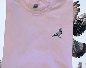 May include: A light pink t-shirt with an embroidered image of a gray pigeon.