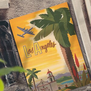 Puede incluir: P&oacute;ster de viaje vintage con fondo amarillo que presenta una palmera, una iglesia y un avi&oacute;n volando por encima. El texto "Los Angeles" est&aacute; escrito en una fuente estilizada.