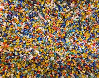 Puede incluir: Una gran colección de pequeñas cuentas de vidrio multicolor en diversas formas y patrones. El surtido presenta tonos vibrantes de amarillo, azul, rojo, verde y blanco, con muchas cuentas que muestran intrincados diseños a rayas o florales.