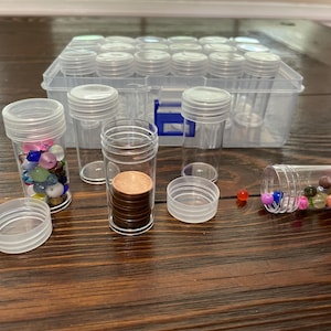 以下が含まれることがあります： 透明なプラスチック製の収納ボックスと、蓋付きの小さな透明なプラスチック製の容器が複数あります。一部の容器には、カラフルなビーズ、コイン、その他の小さなアイテムが入っています。