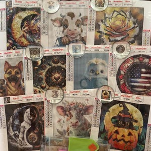 May include: A collection of diamond painting kits featuring various designs, including a cow, a rose, a pumpkin, and a dog. Each kit is labeled with an item number and size, 20x20cm. The kits are displayed with round, clear magnets.