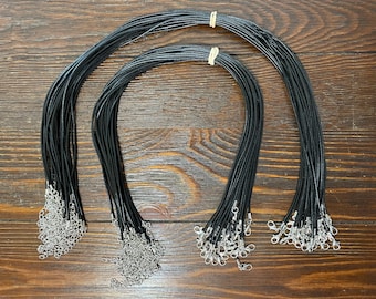 May include: A set of black cord necklaces with silver clasps. The cords are bundled together and arranged in three groups.