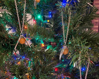 May include: Several silver chain necklaces with a golden orb pendant and silver wings are displayed on a Christmas tree. The tree is decorated with colorful lights, creating a festive and magical atmosphere.