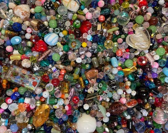 Puede incluir: Una gran colección de cuentas artesanales variadas en una amplia gama de formas, tamaños y colores. La mezcla incluye acabados transparentes, opacos, translúcidos y metálicos, con cuentas redondas, facetadas, en forma de corazón y rectangulares.