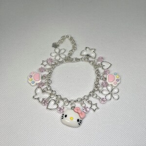 May include: A silver charm bracelet with pink and white charms, including a Hello Kitty charm, paw print charms, flower charms, and star charms.