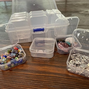 May include: A set of clear plastic storage containers with lids. The containers are various sizes and are filled with small items, such as beads, jewelry, and other craft supplies.