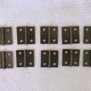 May include: Ten antique-style, small, metal hinges in a row. The hinges are a dark brown color and have a slightly distressed finish.