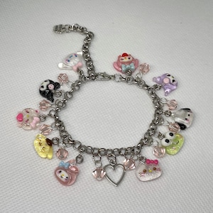 May include: A silver-toned charm bracelet featuring various colorful, cartoon-style charms. Charms include a heart, a cat, a bear, and other cute characters. The bracelet is approximately 7 inches in length.