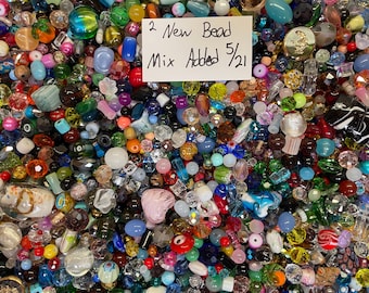 May include: A vibrant assortment of colorful beads in various shapes and sizes. The mix includes glass, crystal, and other materials in shades of red, blue, green, and more. A small white card reads "2 New Bead Mix Added 5/21".