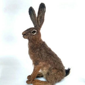 May include: A brown and gray needle felted hare sculpture. The hare is sitting with its ears upright and its tail tucked behind its legs.
