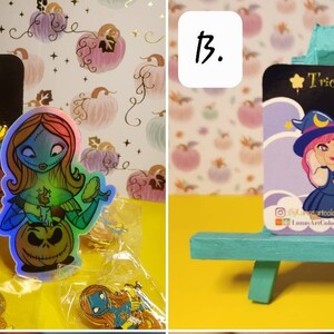 May include: Two Halloween-themed enamel pins on a small easel. The first pin features a witch with a cauldron and a ghost. The second pin features a witch with a cauldron and a skeleton.