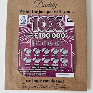 May include: A greeting card with a lottery scratch-off ticket. The card is brown with the word "Daddy" at the top. The scratch-off ticket is purple and features the text "10X" and "&pound;100,000". The card includes the message "We hit the jackpot with you..." and "Love from Rosie & Teddy x".