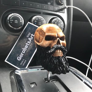 Op de afbeelding: Een pookknop in de vorm van een schedel met een zwarte baard. De knop is gemaakt van hars en is een unieke en stijlvolle manier om persoonlijkheid aan je auto toe te voegen.