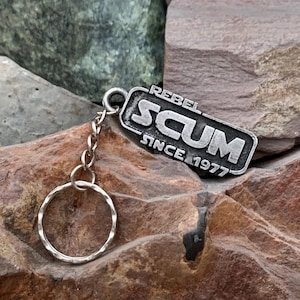 May include: A silver keychain with a rectangular tag that reads "Rebel Scum Since 1977".