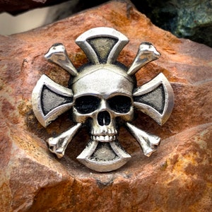 May include: A silver skull and crossbones pendant with a detailed design. The skull has a prominent nose and eye sockets.