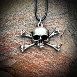 May include: A silver skull and crossbones pendant on a black cord necklace.