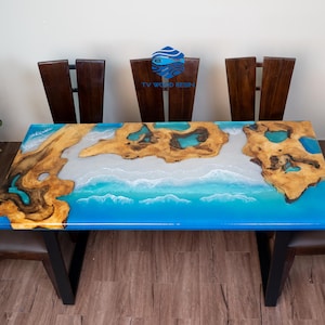 May include: A rectangular dining table with a blue epoxy resin top, featuring a wave design and wooden accents. The table is supported by black legs and surrounded by four wooden chairs. The table's dimensions are approximately 60 inches long and 30 inches wide.